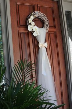 a wedding dress hanging on a door with flowers in the front and behind it is a potted plant