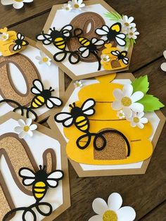 four bee themed birthday cards on a table with paper flowers and glittered letters that spell out the number six