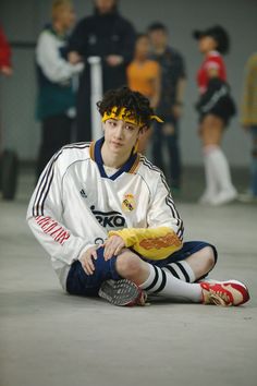 a young man sitting on the ground with his foot up in front of him and people standing behind him