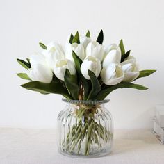 white tulips in a clear glass vase on a table next to a stack of books