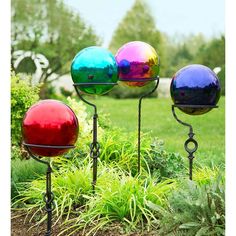 three colorful balls are on top of metal poles in the grass near bushes and trees