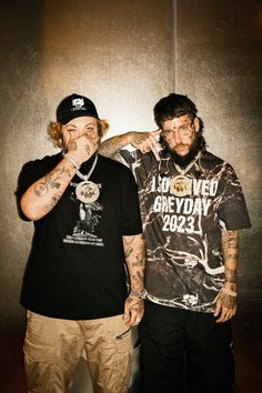 two men standing next to each other in front of a wall with tattoos on it