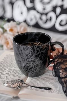 a black coffee cup sitting on top of an open book next to a lace garter