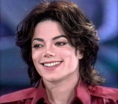 a close up of a person wearing a red shirt and smiling at the camera with long hair