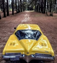 an old yellow car parked on the side of a dirt road in front of trees