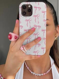 a woman holding up her phone case with pink bows and pearls on the front, while wearing