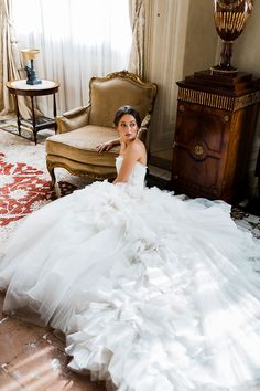 a woman in a wedding dress sitting on the floor next to a chair and window