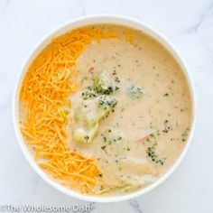 broccoli cheese soup in a white bowl on a marble counter top with shredded cheese