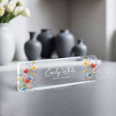 a glass name plate with flowers on it sitting on a table next to vases