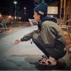 a young man squatting on the ground in front of a building at night with his hand out