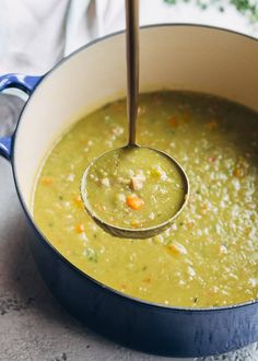 a ladle full of soup being stirred by a wooden spoon in a blue pot