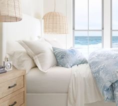 a bed with white sheets and pillows next to an ocean view from a bedroom window