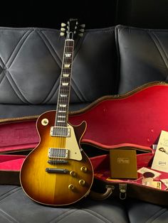 an electric guitar sitting on top of a black leather couch next to a red case