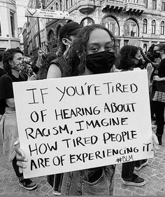 a woman holding a sign that says if you're tired of hearing about racism, imagine how tired people are of experiencing it