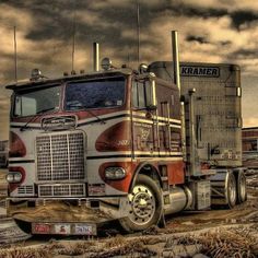 a large semi truck parked on top of a dry grass covered field in front of a cloudy sky