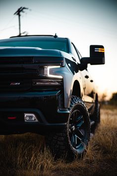 the front end of a black truck parked on top of a dry grass covered field