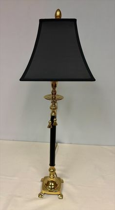 a lamp with a black shade on top of it and a gold plated base