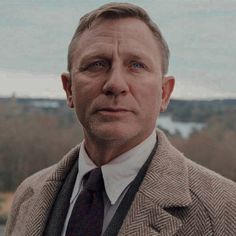 a man in a suit and tie looking off into the distance with trees in the background