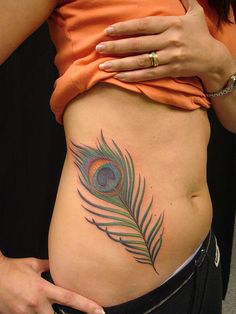 a woman's stomach with a peacock feather tattoo on her belly and an orange tank top