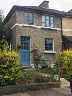 a blue door is in front of a grey brick house with plants and flowers around it