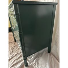 a green dresser with drawers on top of white sheeted floor next to a mirror