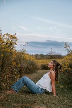 a woman sitting in the grass with her eyes closed and looking up to the sky