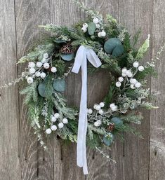 a wreath with white flowers and greenery hanging on a wooden wall next to a fence