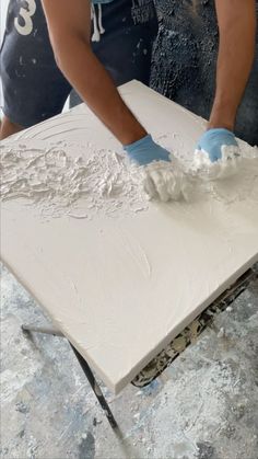 two people with gloves on painting a piece of white art work in an art studio