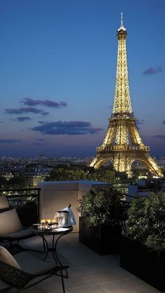 the eiffel tower is lit up at night, with tables and chairs around it