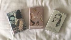 three cassettes are laying on a bed with white sheets and one has an image of a woman's face