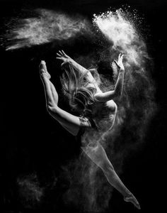 a black and white photo of a ballerina in the air with powder behind her