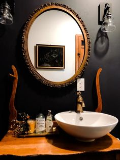 a bathroom sink sitting under a mirror next to a wall mounted faucet in front of a painting