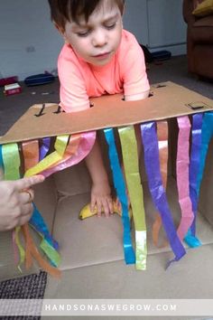 a young child sitting in a cardboard box with streamers on the floor next to it