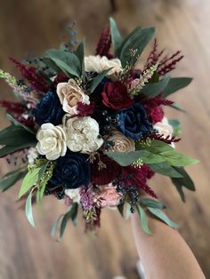 a bridal bouquet with red, white and blue flowers is held by someone's hand