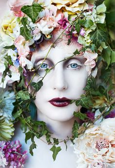 a woman with flowers on her head is surrounded by greenery and pink roses in front of her face