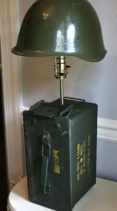 an army green lamp is on top of a black box in front of a white wall