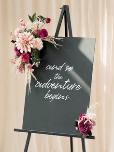 a sign with flowers on it that says, and so the adventure begins next to an easel