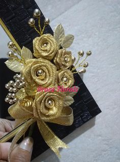 a person is holding a gold colored flower with pearls and leaves on it while wearing a black card case