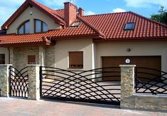 a house with an iron gate and brick driveway in the foreground, on a sunny day