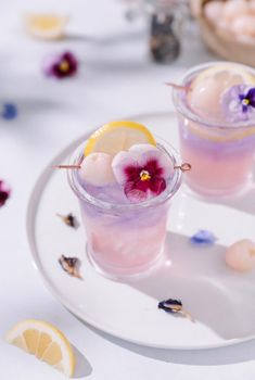 two glasses filled with drinks sitting on top of a white plate next to lemon slices