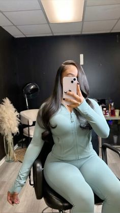 a woman sitting in a chair taking a selfie with her cell phone while wearing a blue outfit