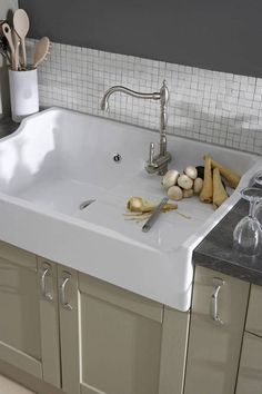 a white kitchen sink sitting under a faucet next to wooden spoons and utensils