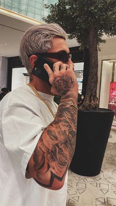 a man with grey hair and tattoos on his arm talking on a cell phone while wearing sunglasses