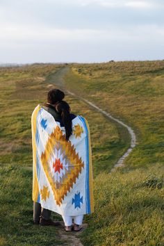 two people wrapped in a blanket standing on a grassy hill with a path leading to the horizon