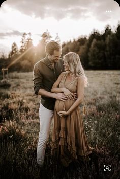 a pregnant couple standing in a field at sunset