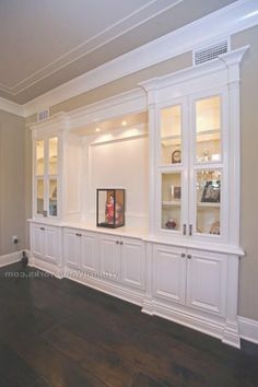 an empty living room with white built in cabinets and dark wood flooring on the walls