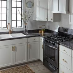 a kitchen with white cabinets, black counter tops and gold trim on the stove top