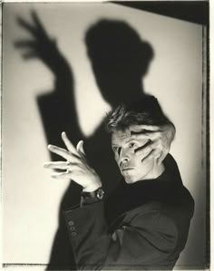 a man with his shadow on the wall behind him, holding his hands up to his face