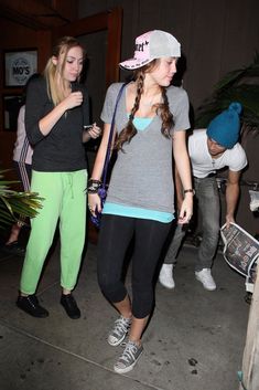 two girls are walking down the sidewalk at night, one is wearing a pink hat