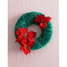 a green wreath decorated with poinsettis on top of a striped table cloth